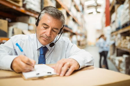 Warehouse manager writing on clipboard in a large warehouseの写真素材