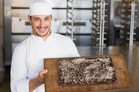 Baker showing freshly baked brownie in the kitchen of the bakeryの写真素材