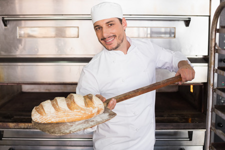 Happy baker taking out fresh loaf in the kitchen of the bakery