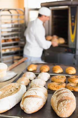 Happy baker taking out fresh loaves in the kitchen of the bakeryの写真素材