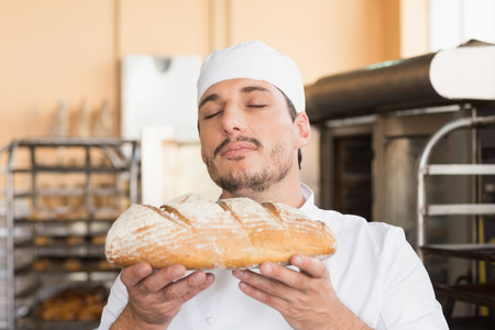 Baker smelling freshly baked loaf in the kitchen of the bakeryの写真素材