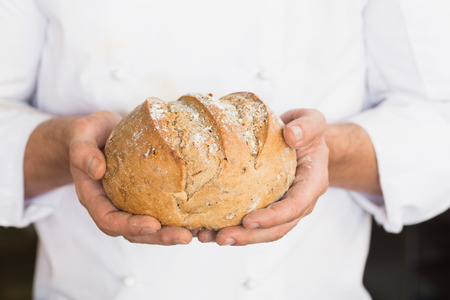 Baker showing freshly baked loaf in the kitchen of the bakery