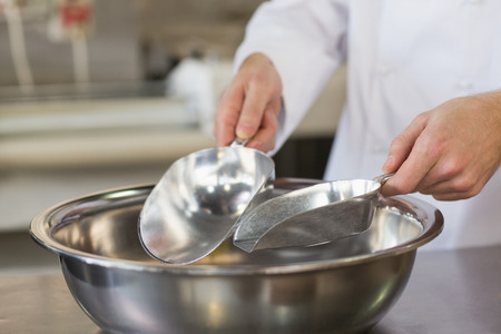 Baker holding scoops over bowl in the kitchen of the bakeryの写真素材