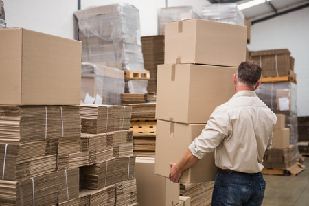 Rear view of worker carrying boxes in warehouseの写真素材