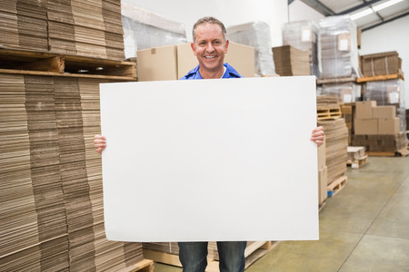Smiling warehouse worker holding large white poster in a large warehouseの写真素材