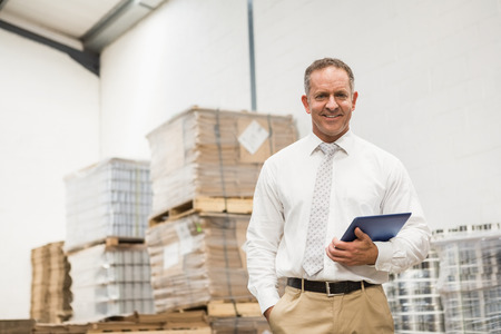 Manager standing with hand in the pocket holding tablet pc in a large warehouseの写真素材