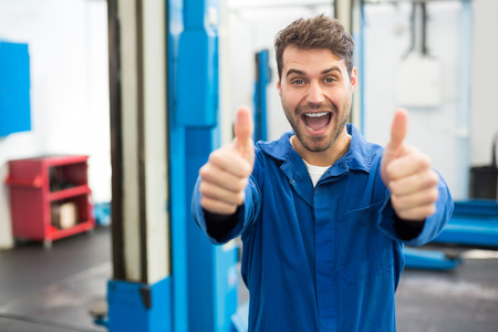 Smiling mechanic showing thumbs up at the repair garageの写真素材