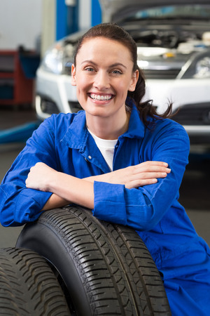 Mechanic smiling at the camera with tire at the repair garageの写真素材