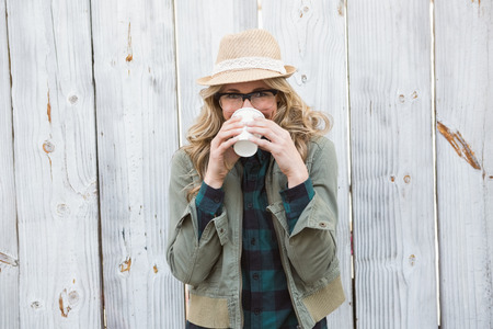 Portrait of blonde drinking from disposable cup against bleached wooden planks