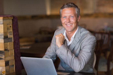 Smiling businessman using his laptop at the cafe