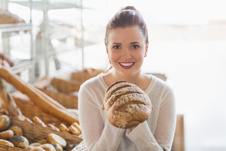 Pretty brunette showing loaf of bread at the bakeryの写真素材