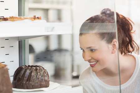 Pretty brunette looking at cake at the bakeryの写真素材