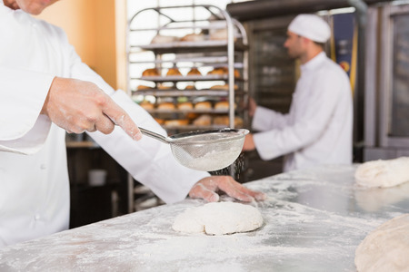 Baker sieving flour on the dough in the kitchen of the bakery