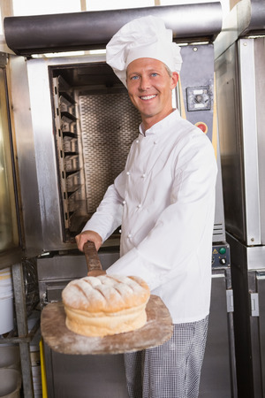 Happy baker taking out fresh loaf in the kitchen of the bakery