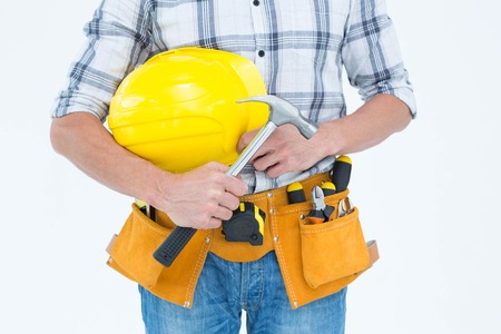 Cropped image of technician holding hammer and hard hat over white background