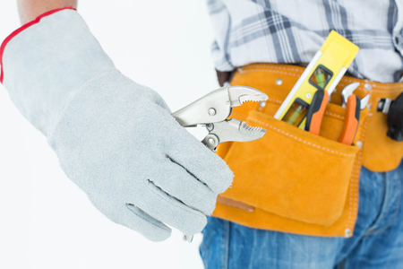 Cropped image of technician with tool belt around waist using pliers over white backgroundの写真素材