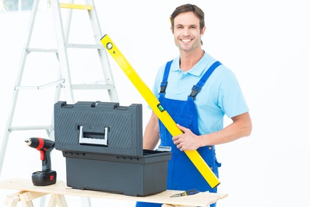 Portrait of happy carpenter holding spirit level at table over white background