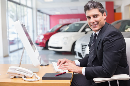 Smiling businessman typing on laptop at new car showroomの写真素材