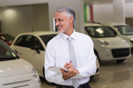 Smiling businessman writing on clipboard at new car showroomの写真素材