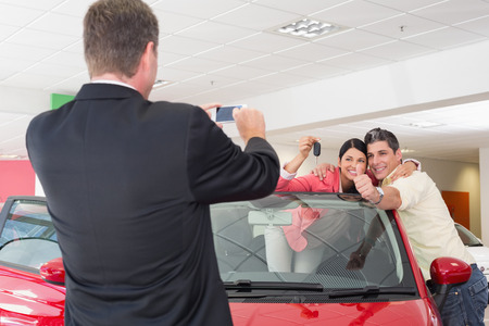 Businessman taking picture of the couple in their new car at new car showroomの写真素材
