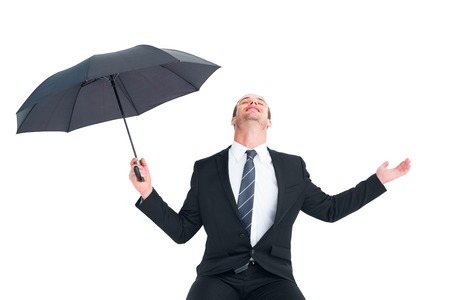 Businessman sheltering under black umbrella testing on white backgroundの写真素材