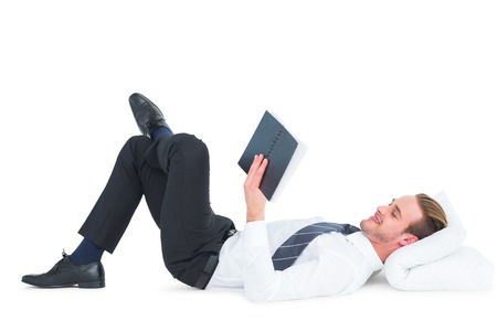 Relaxed businessman lying and reading book on white backgroundの写真素材
