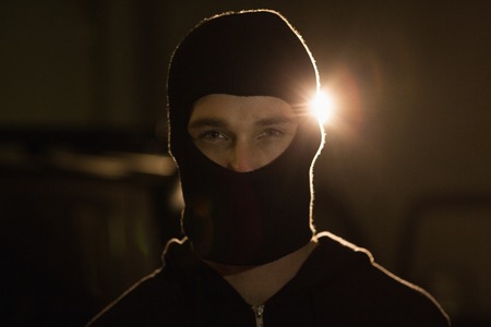 Criminal in balaclava looking at camera in a shadowy settingの写真素材