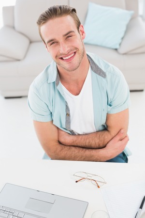 Smiling businessman with arms crossed at his desk in the officeの写真素材