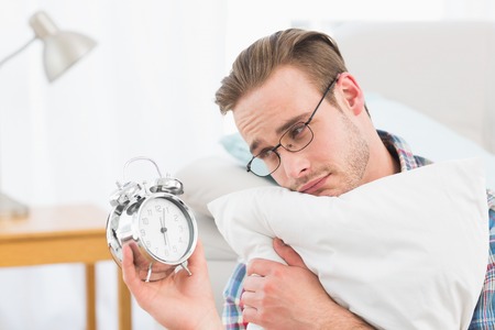 Bored man holding alarm clock at home in the living roomの写真素材
