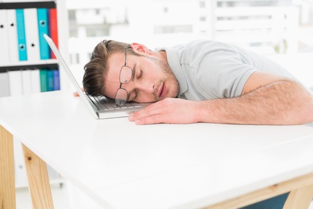 Tired businessman resting on laptop in his officeの写真素材