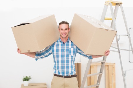Smiling man carrying cardboard moving boxes at home in the living roomの写真素材