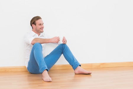 Casual man sitting on floor holding cup at home in the living roomの写真素材