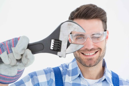 Portrait of confident repairman wearing protective glasses while holding wrench on white backgroundの写真素材