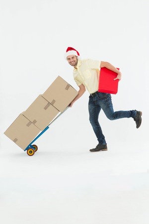 Full length portrait of delivery man pushing trolley of boxes during Christmas on white backgroundの写真素材