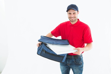 Portrait of happy delivery man removing pizza box from bag on white backgroundの写真素材