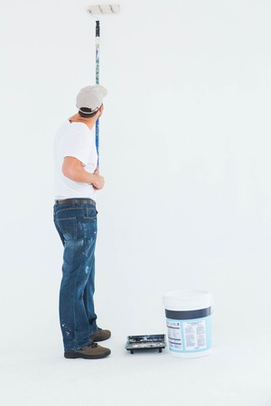 Full length rear view of man using paint roller on white backgroundの写真素材