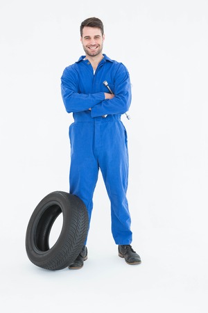 Full length portrait of smiling young male mechanic with arms crossed standing by tire on white backgroundの写真素材