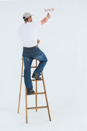 Full length rear view of man on ladder painting with roller over white backgroundの写真素材
