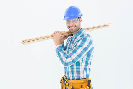 Portrait of happy construction worker carrying wooden planks against white background