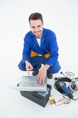 Portrait of smiling construciton worker pointing at laptop against white backgroundの写真素材