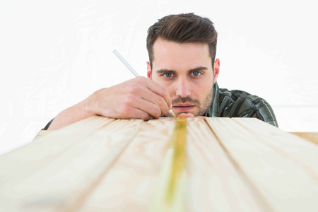 Male carpenter marking on wooden plank against white backgroundの写真素材