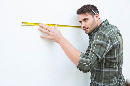 Side view of male carpenter measuging white wall with measure tape at homeの写真素材
