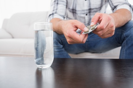 Hungover man with his medicine laid out on coffee table at home in the living roomの写真素材