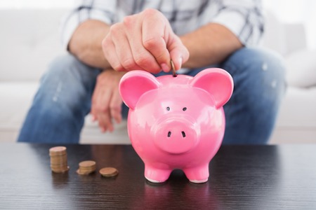 A man putting coins in piggy bank at home in the living roomの写真素材