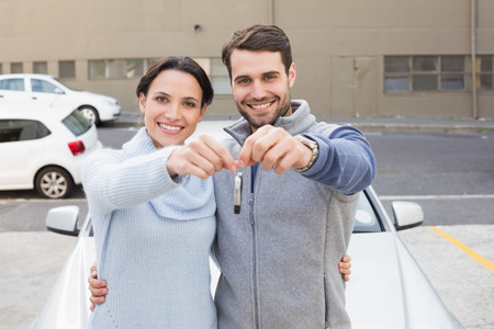Young couple smiling holding new key outside their carの写真素材