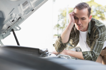 Upset man checking his car engine after breaking down in a car park