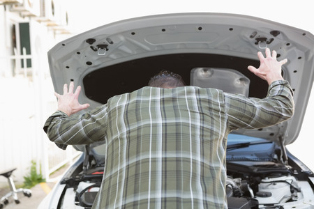 Angry man checking his car engine after breaking down in a car parkの写真素材