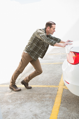 Man pushing his broken down car in a car parkの写真素材