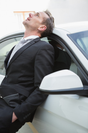 Upset businessman leaning on his car in a car parkの写真素材