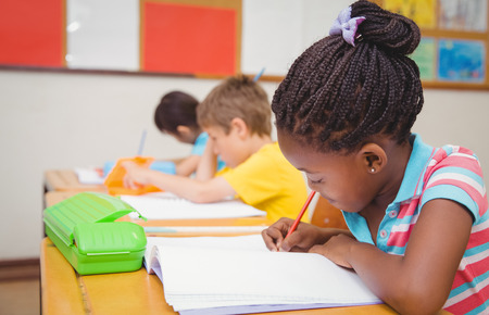 Cute pupils writing at desk in classroom at the elementary schoolの写真素材